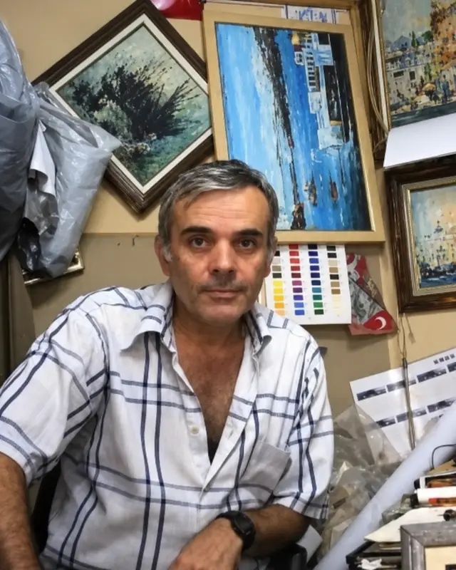 Portrait of oil painter Naci Caba in his studio, surrounded by his paintings